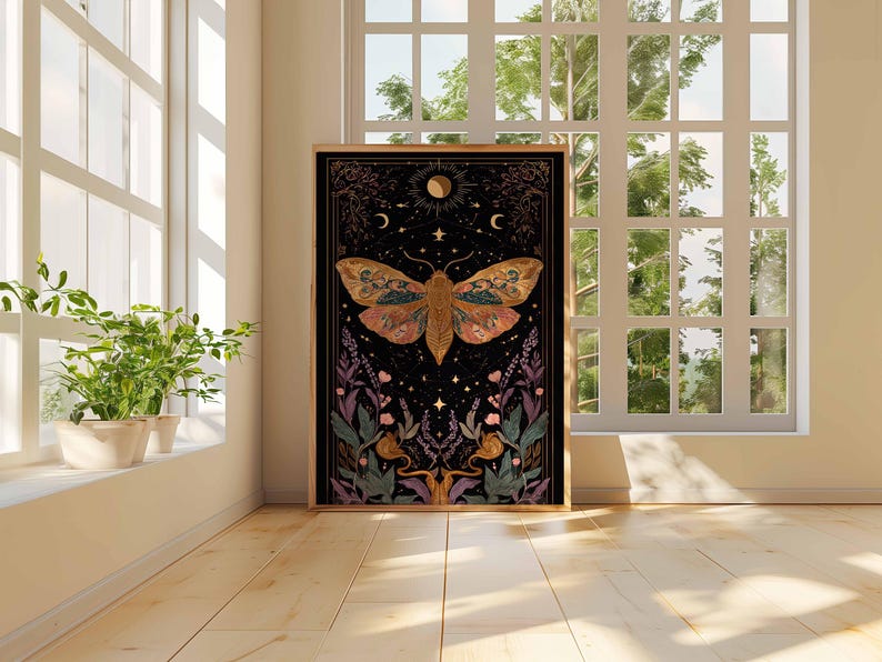 May include: A framed art print featuring a detailed illustration of a moth with intricate wing patterns in shades of orange, brown, and gold. The artwork is set against a black background with celestial elements and floral accents. The print is displayed in a room with natural light.