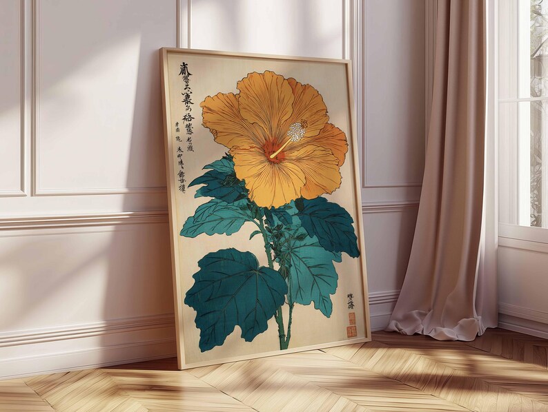 May include: A framed botanical print of a large yellow hibiscus flower with a red centre and green leaves. The artwork includes Japanese text and is set against a beige background. The frame is light wood, and the print leans against a white wall.