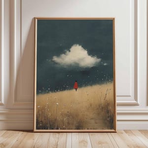 May include: A framed art print depicting a figure in a red cloak on a grassy hill beneath a dark, cloudy sky. The artwork has a minimalist style with a muted colour palette, creating a sense of solitude. The print is presented in a wooden frame.