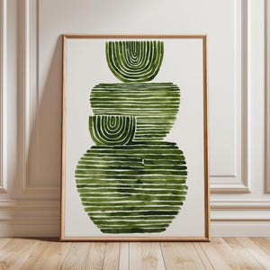 Può includere: Stampa artistica astratta con un design impilato di forme verdi ad acquerello. L'opera d'arte è incorniciata in una sottile cornice di legno colorata. Le forme sono composte da linee orizzontali ed elementi a forma di semicerchio, creando un'estetica moderna e minimalista.
