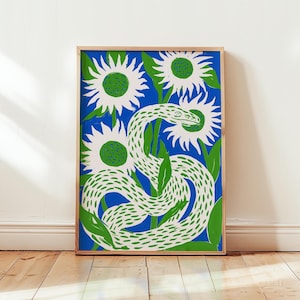 May include: A rectangular art print in a light wood frame featuring a white snake with green spots coiled among three large white sunflowers with green centers, all set against a vibrant blue background with green leaves and stems.