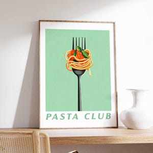 Op de afbeelding: Een ingelijste print met een zwarte vork met spaghetti, tomatensaus en basilicum tegen een lichtgroene achtergrond. De woorden "PASTA CLUB" staan in het groen onderaan. De print wordt getoond op een houten plank.