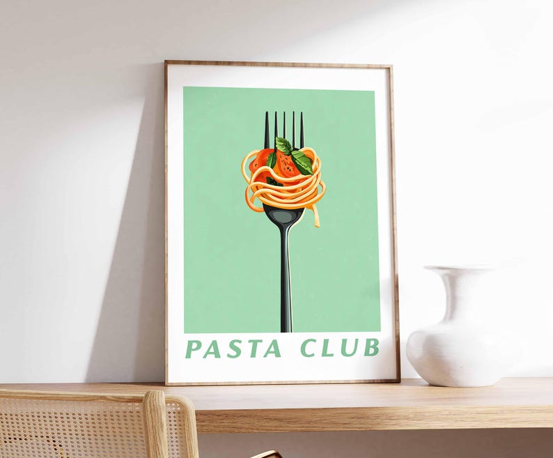 Op de afbeelding: Een ingelijste print met een zwarte vork met spaghetti, tomatensaus en basilicum tegen een lichtgroene achtergrond. De woorden "PASTA CLUB" staan in het groen onderaan. De print wordt getoond op een houten plank.