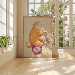 K&ouml;nnte beinhalten: Ein gerahmter Kunstdruck zeigt eine gro&szlig;e orange Katze auf einem kleinen blauen Fahrrad mit einem rosa Rad. Die Katze l&auml;chelt. Das Kunstwerk wird in einem Raum mit Fenster und Pflanzen ausgestellt.