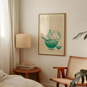 May include: A framed wall art print featuring a green line drawing of a cat eating noodles from a bowl with chopsticks. The illustration is set against a light beige background, capturing the cat leaning over the bowl with steam rising.