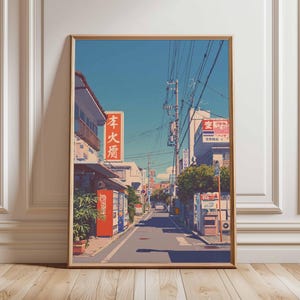 Könnte beinhalten: Gerahmter Druck einer japanischen Straßenszene mit Gebäuden, Strommasten und einem klaren blauen Himmel. Das Kunstwerk zeigt einen roten Coca-Cola-Automaten und Schilder mit japanischen Schriftzeichen. Der Stil erinnert an Anime oder Vintage-Reiseposter.