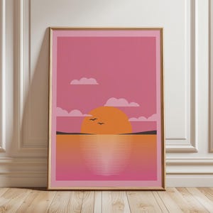 Op de afbeelding: Ingelijste kunstdruk met een zonsondergangscène. Het kunstwerk toont een grote oranje zon die ondergaat boven water, met vogels die eroverheen vliegen. De lucht is een verloop van roze en oranje, met witte wolken. De print zit in een gouden lijst.