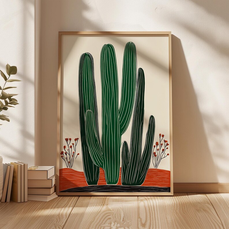 May include: A framed art print featuring a stylized illustration of green cacti with white vertical lines against a cream background. The artwork includes a red-orange desert floor and small red flowering plants. The frame is a light wood color.