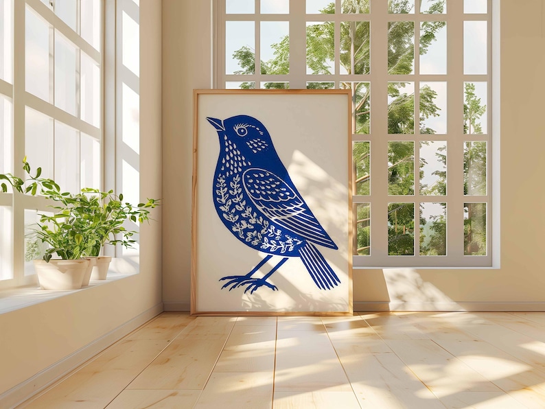 May include: A framed art print featuring a blue bird illustration with white leaf-like patterns. The artwork is displayed in a bright room with a window and potted plants. The bird is standing, facing left.