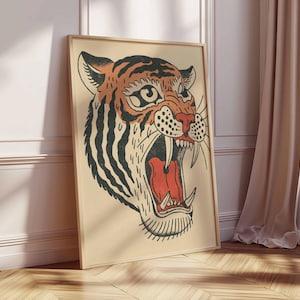 May include: Framed art print featuring a tiger's head with an open mouth, showcasing sharp teeth and a red interior. The tiger has orange and black stripes, with a beige background. The artwork is in a wooden frame, leaning against a wall.