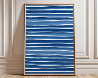 May include: A framed abstract art print featuring horizontal blue and white stripes. The artwork has varying shades of blue, creating a textured appearance. The frame is a light brown color, and the artwork is displayed against a white wall.