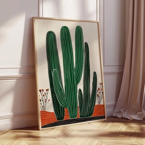 May include: A framed art print featuring a stylized illustration of green cacti with white vertical lines against a cream background. The cacti stand on a red and black base, with small red floral accents. The artwork is displayed in a light wood frame.