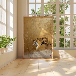 K&ouml;nnte beinhalten: Ein gerahmtes Kunstwerk mit einem Tiger, der durch eine goldfarbene Landschaft mit Bambus geht. Der Tiger hat schwarze Streifen auf orangefarbenem Fell. Das Kunstwerk wird in einem Raum mit Fenster und Pflanzen ausgestellt.