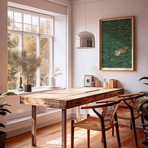 May include: A bright, airy room with a wooden desk and two chairs. A framed print of a tiger swimming in green water hangs on the wall. The room has a large window with a view of trees and a decorative hanging light.