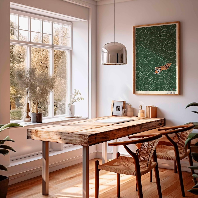 May include: A bright, airy room with a wooden desk and two chairs. A framed print of a tiger swimming in green water hangs on the wall. The room has a large window with a view of trees and a decorative hanging light.