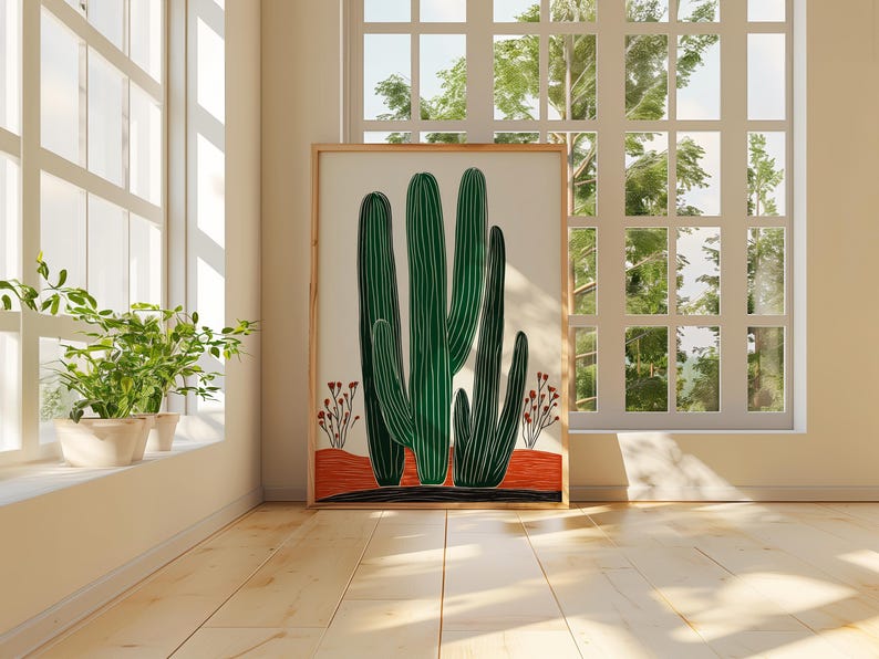 May include: A framed art print featuring a stylized illustration of green cacti against a cream background. The artwork includes a red and black base with small red floral accents. The print is displayed in a bright room with a window.