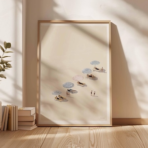 May include: A framed art print showing a beach scene with sun loungers, striped parasols, and small figures. The artwork has a minimalist style with a neutral colour palette, creating a calm and relaxing atmosphere. The print is displayed against a light-coloured wall.