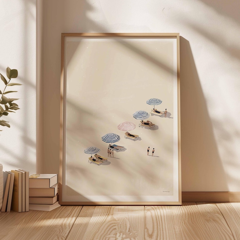 May include: A framed art print showing a beach scene with sun loungers, striped parasols, and small figures. The artwork has a minimalist style with a neutral colour palette, creating a calm and relaxing atmosphere. The print is displayed against a light-coloured wall.