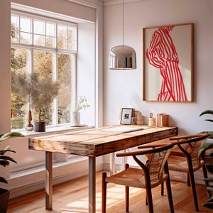 Puede incluir: Una habitaci&oacute;n luminosa con un escritorio de madera y dos sillas. Una obra de arte enmarcada con rayas rojas y blancas cuelga de la pared. Una gran ventana ofrece vistas a los &aacute;rboles. Una l&aacute;mpara colgante plateada cuelga sobre el escritorio.