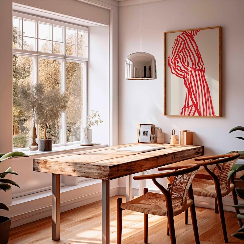 Puede incluir: Una habitaci&oacute;n luminosa con un escritorio de madera y dos sillas. Una obra de arte enmarcada con rayas rojas y blancas cuelga de la pared. Una gran ventana ofrece vistas a los &aacute;rboles. Una l&aacute;mpara colgante plateada cuelga sobre el escritorio.