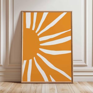 May include: A framed abstract art print with a striking design. The artwork displays a bright orange background with white, sunburst-like shapes emanating from the left. The print is in a simple wooden frame, suitable for wall decor.