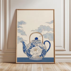 Puede incluir: Impresión artística enmarcada que muestra una tetera azul y blanca con diseño floral y asa dorada. La tetera se sitúa sobre un fondo de nubes celestes. La obra está enmarcada en madera.