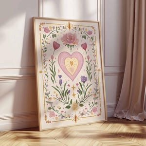 May include: A framed art print featuring a central heart design with a smaller heart inside, surrounded by floral elements in pink, purple, and green. The artwork is set against a cream background with a wooden frame.