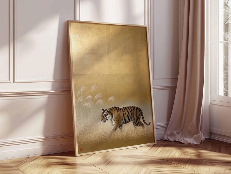 May include: Framed art print featuring a tiger walking through tall grass. The artwork has a gold background with a sepia-toned tiger and grass. The frame is a light wood color. The artwork is leaning against a white wall and a beige curtain.