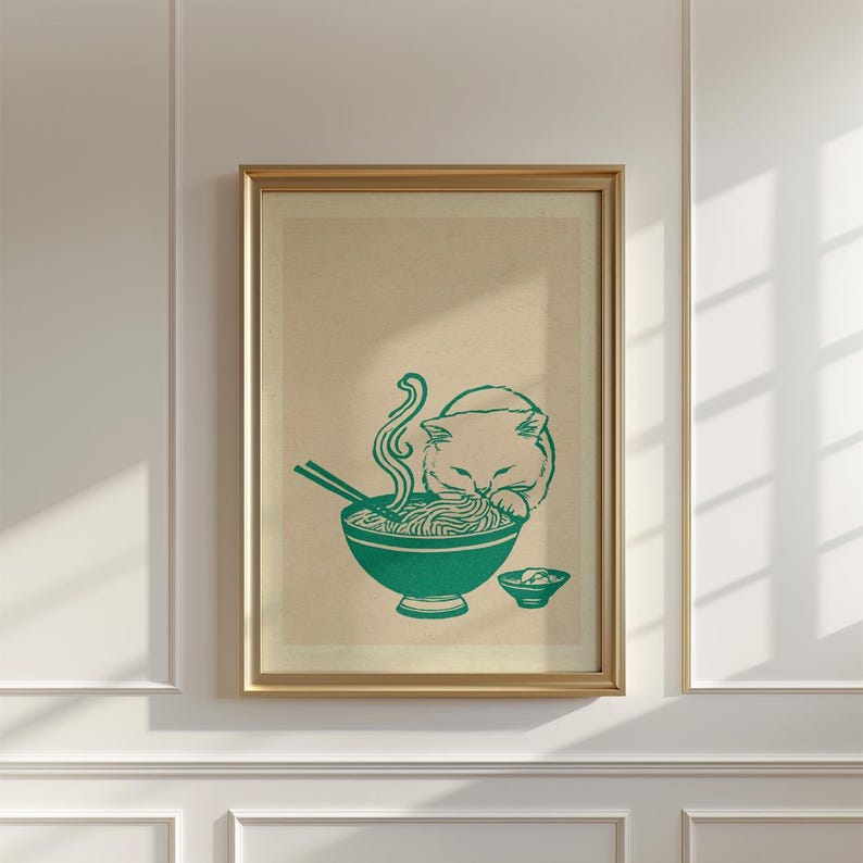 May include: A framed wall art print featuring a dark green line drawing of a cat eating noodles from a bowl with chopsticks. The illustration is set against a light beige background, capturing the cat leaning over the steaming bowl of food.