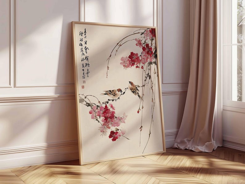 Peut inclure: Une impression d'art encadr&eacute;e repr&eacute;sentant une peinture d'inspiration asiatique. L'&oelig;uvre d'art montre deux oiseaux perch&eacute;s sur une branche fleurie avec des fleurs rouges. De la calligraphie est visible. Le cadre est en bois clair.