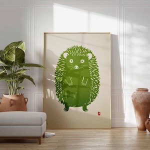 Pu&ograve; includere: Una grande stampa incorniciata con un'illustrazione di un riccio verde. L'opera d'arte ha uno stile minimalista con uno sfondo beige chiaro e un piccolo quadrato rosso in basso a destra. La stampa &egrave; esposta in una stanza con una pianta, un pouf e vasi decorativi.