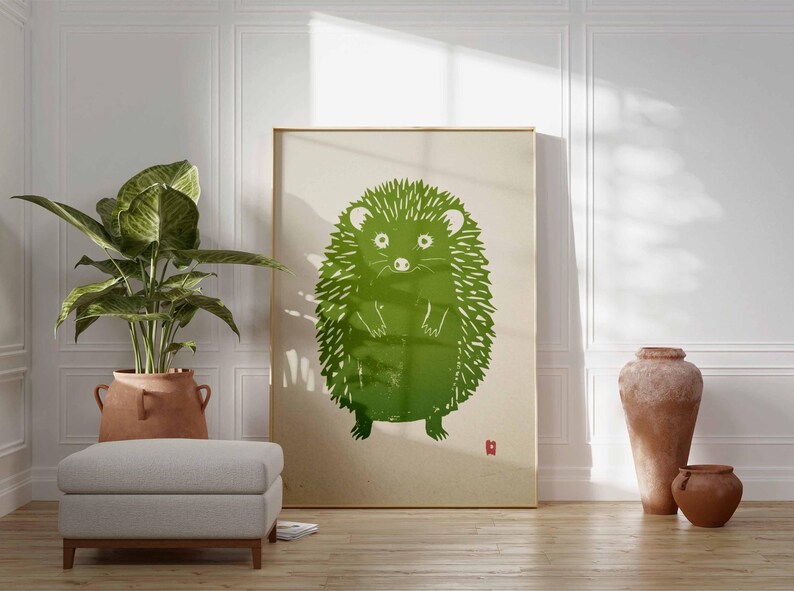 Pu&ograve; includere: Una grande stampa incorniciata con un'illustrazione di un riccio verde. L'opera d'arte ha uno stile minimalista con uno sfondo beige chiaro e un piccolo quadrato rosso in basso a destra. La stampa &egrave; esposta in una stanza con una pianta, un pouf e vasi decorativi.