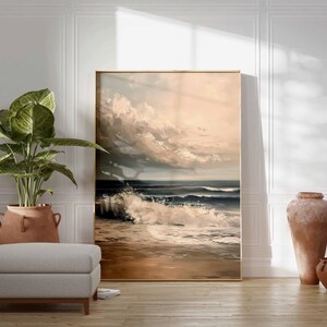 May include: A framed landscape painting depicts a dramatic ocean scene with crashing waves and a cloudy sky. A large potted plant, a gray ottoman, and two terracotta vases are in the foreground, creating a serene interior design.