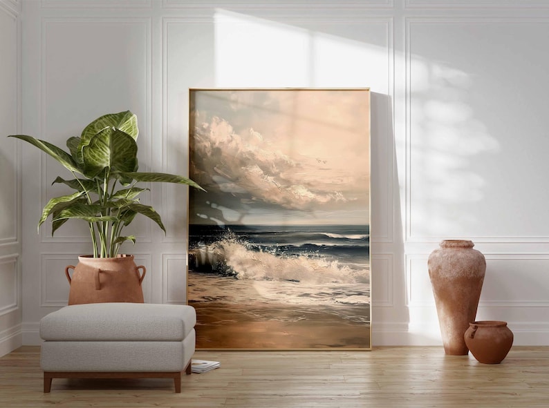 May include: A framed landscape painting depicts a dramatic ocean scene with crashing waves and a cloudy sky. A large potted plant, a gray ottoman, and two terracotta vases are in the foreground, creating a serene interior design.