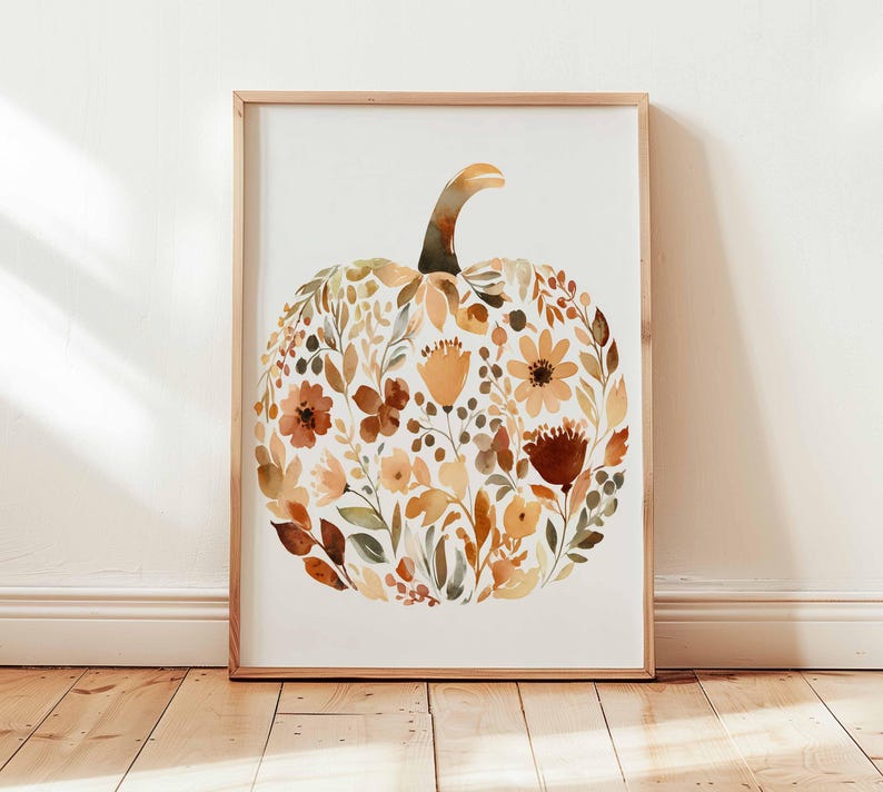 May include: A framed watercolor print featuring a pumpkin shape composed of autumn-colored flowers and foliage. The artwork has a light wooden frame and is displayed against a white background. The color palette includes shades of orange, brown, and green.