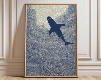 May include: A framed art print featuring a navy blue shark leaping from stylized ocean waves. The artwork has a textured, linocut style with a light beige sky. The print is displayed in a natural wood frame, suitable for coastal or nautical decor.