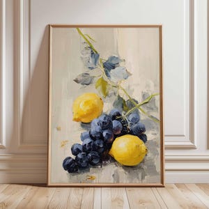 May include: A framed still life painting of yellow lemons and dark blue grapes. The artwork has a light background with blue and green foliage. The painting is in a wooden frame and leans against a white wall and wooden floor.
