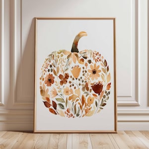 May include: A framed watercolor print featuring a pumpkin shape composed of autumn-toned flowers and foliage. The artwork showcases shades of orange, brown, and yellow, with a light background and a wooden frame.