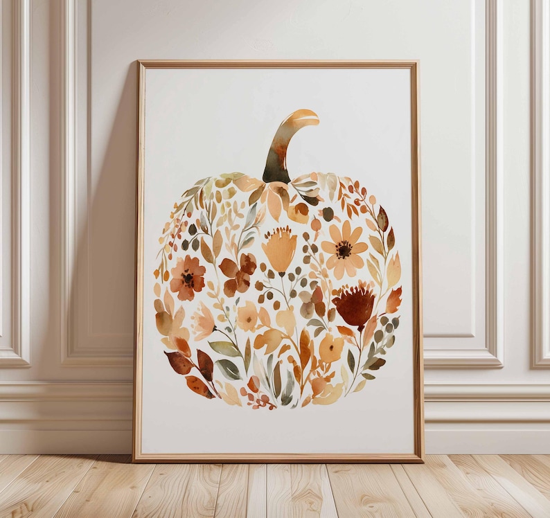 May include: A framed watercolor print featuring a pumpkin shape composed of autumn-toned flowers and foliage. The artwork showcases shades of orange, brown, and yellow, with a light background and a wooden frame.