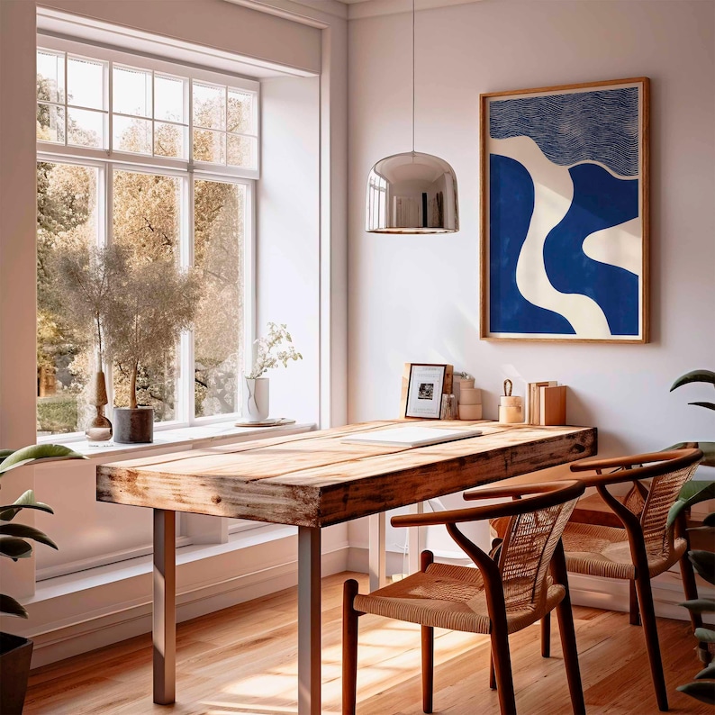 Puede incluir: Una habitaci&oacute;n luminosa con un escritorio de madera y dos sillas. Una obra de arte abstracta enmarcada en azul y blanco cuelga de la pared. Una gran ventana ofrece vistas a los &aacute;rboles. Una l&aacute;mpara colgante plateada cuelga sobre el escritorio.