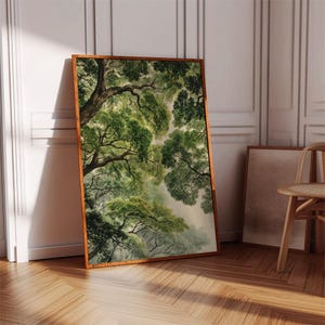 May include: A framed art print featuring a watercolor painting of a forest canopy. The artwork showcases lush green foliage and tree branches, with a warm brown wooden frame. The print is leaning against a white wall and wooden floor.