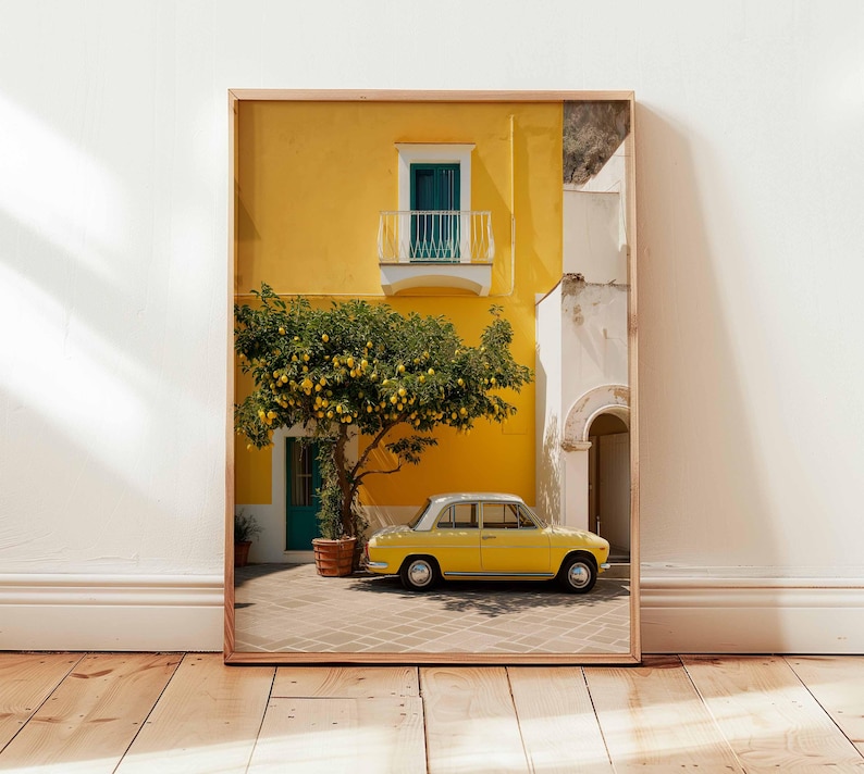 May include: Framed print of a yellow building with a teal door and balcony, a lemon tree, and a yellow vintage car. The building has a white section and a brown wooden frame. The scene is set on a brick patio.