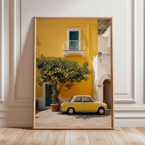 May include: Framed print featuring a yellow building with a teal door and balcony. A lemon tree laden with fruit stands in front of the building, and a vintage yellow car is parked nearby. The scene is set on a brick patio.