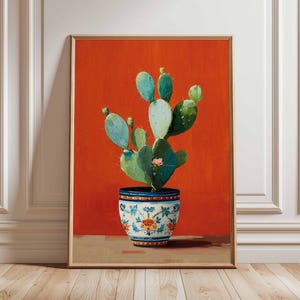 Puede incluir: Pintura enmarcada de un cactus en una maceta decorativa. El cactus tiene almohadillas de color verde claro y verde oscuro con una pequeña flor rosa. La maceta es azul y blanca con un diseño floral, sobre un fondo naranja vibrante.