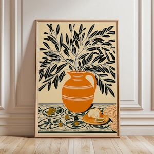 May include: A framed wall art print featuring an orange pitcher filled with dark green olive branches. The pitcher sits on a surface with a patterned tile design, scattered olives, a small plate with bread slices, and a striped cloth napkin.