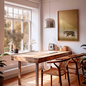 May include: A bright, airy home office with a large wooden desk and two woven chairs. A framed tiger art piece hangs on the wall. A large window offers a view of the outdoors. A modern chrome pendant light hangs above the desk.