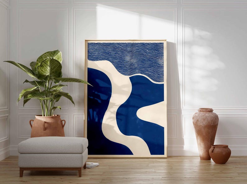 Puede incluir: Impresi&oacute;n art&iacute;stica abstracta en un marco de madera. La obra de arte presenta un dise&ntilde;o con formas azules y blanquecinas. Una gran planta en maceta, un otom&aacute;n gris y jarrones de terracota est&aacute;n en primer plano, creando un dise&ntilde;o interior moderno.