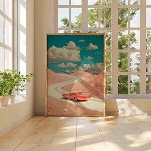 K&ouml;nnte beinhalten: Ein gerahmter Kunstdruck mit einem Oldtimer in Orange auf einer kurvenreichen Stra&szlig;e durch eine bergige Landschaft unter einem bew&ouml;lkten Himmel. Das Kunstwerk hat eine Retro-&Auml;sthetik mit einer Farbpalette aus Orange, T&uuml;rkis und Rosa.