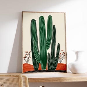 May include: A framed art print featuring a stylized illustration of green cacti against a cream background. The cacti are set on a red-orange ground with small red flowering plants. The frame is a light brown color.