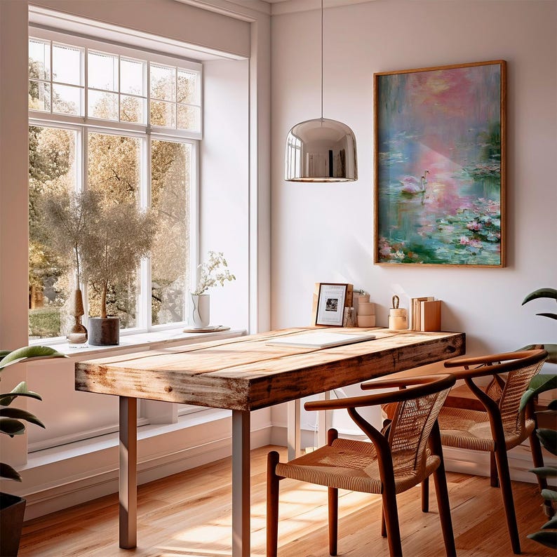 May include: A home office with a large wooden desk, two woven chairs, and a framed painting of a lake scene. A large window offers a view of trees. A silver pendant light hangs above the desk.